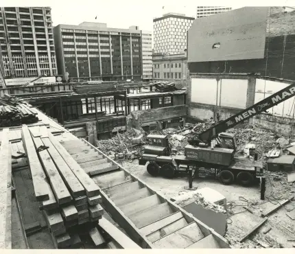 Construction site in an urban area with cranes and machinery, surrounded by tall buildings.