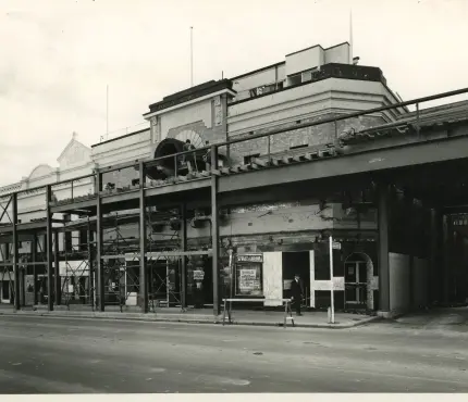Black and white photo of a building undergoing construction or renovation, with scaffolding and steel beams in front.