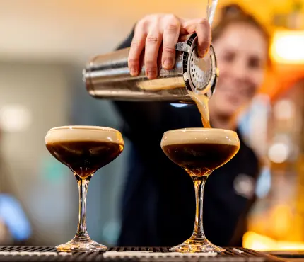 Bartender pouring espresso martinis into glasses.