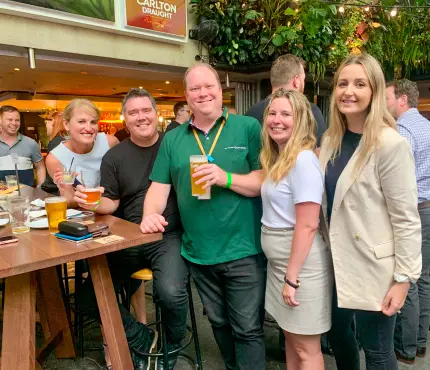 Group of people smiling and holding drinks at an outdoor bar.